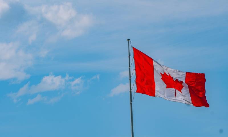 A Canadian flag flying with a blue sky background.