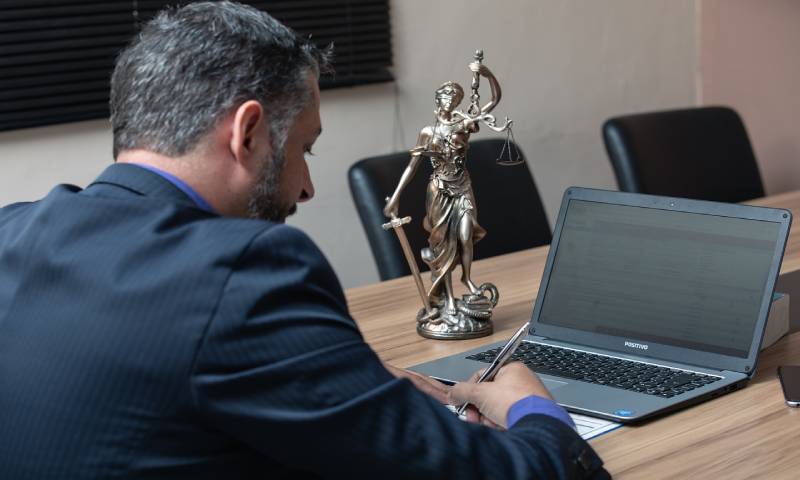 A lawyer writes a letter on a laptop as the justice statue stands behind them