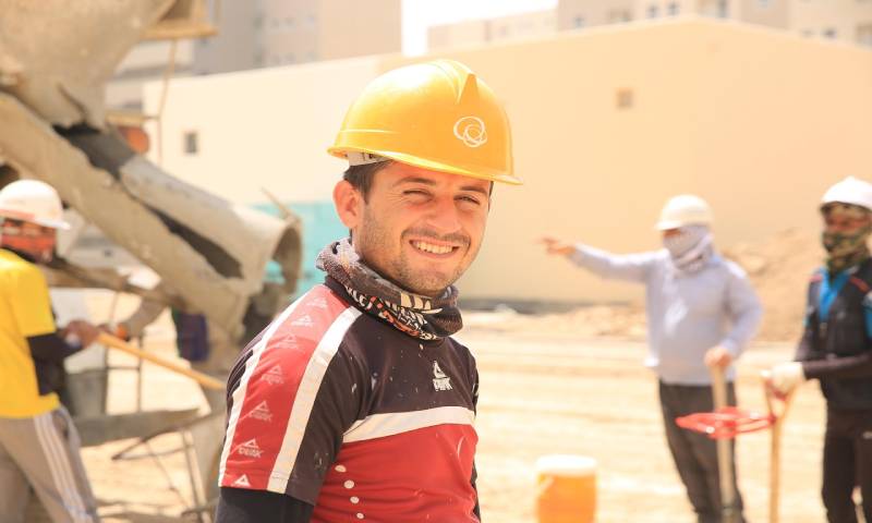 A construction worker smiling as work happens behind them.