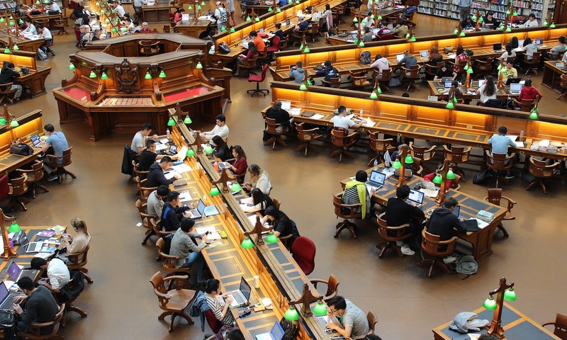 Students study at long desks in a large university library reading room.