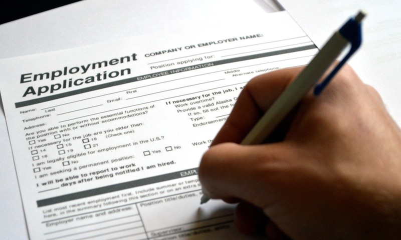 A hand holding a pen fills out a paper application form.